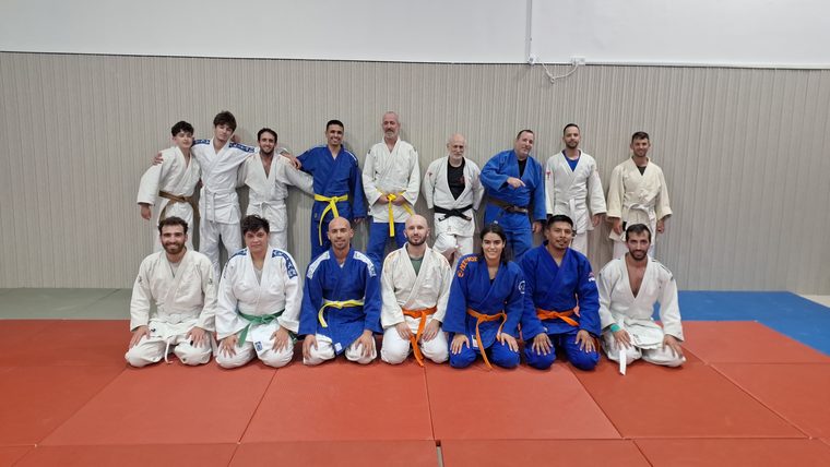 קבוצת ג׳ודופאן מצטלמת יחד באולם האימונים, מתאמנים בחגורות בצבעים שונים בשורה עומדת ושורה כורעת